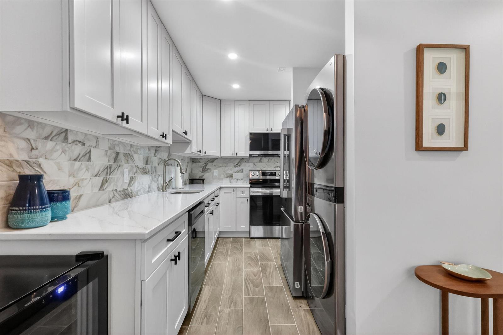 A galley kitchen features white cabinets, marble-style backsplash, stainless steel appliances, and wood-look tile flooring — 1101 Cactus Terrace # 204, Delray Beach FL 33445, DELRAY BEACH, FL