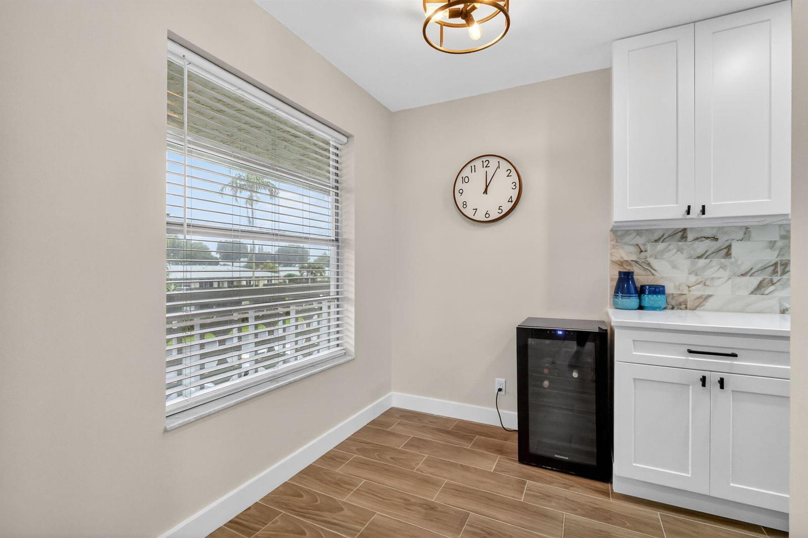 A kitchen nook features white cabinets, a wine cooler, a wall clock, and wood-look flooring — 1101 Cactus Terrace # 204, Delray Beach FL 33445, DELRAY BEACH, FL