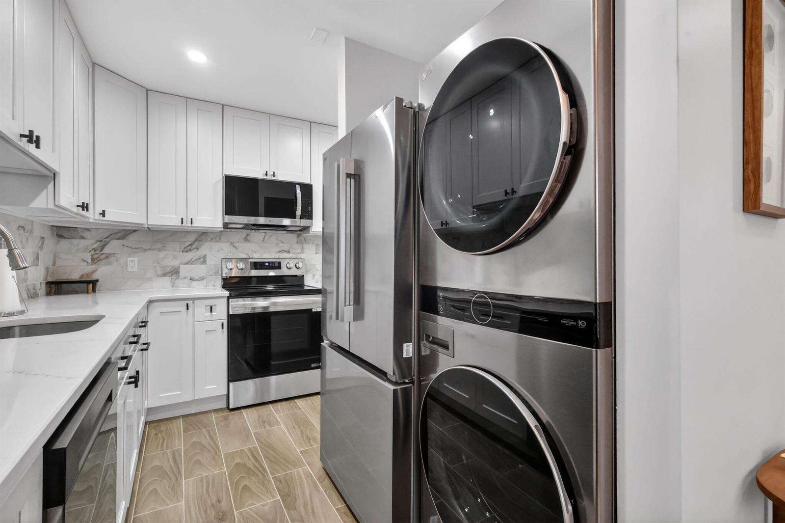 A modern kitchen features white cabinets, stainless steel appliances, and a stacked washer-dryer unit — 1101 Cactus Terrace # 204, Delray Beach FL 33445, DELRAY BEACH, FL