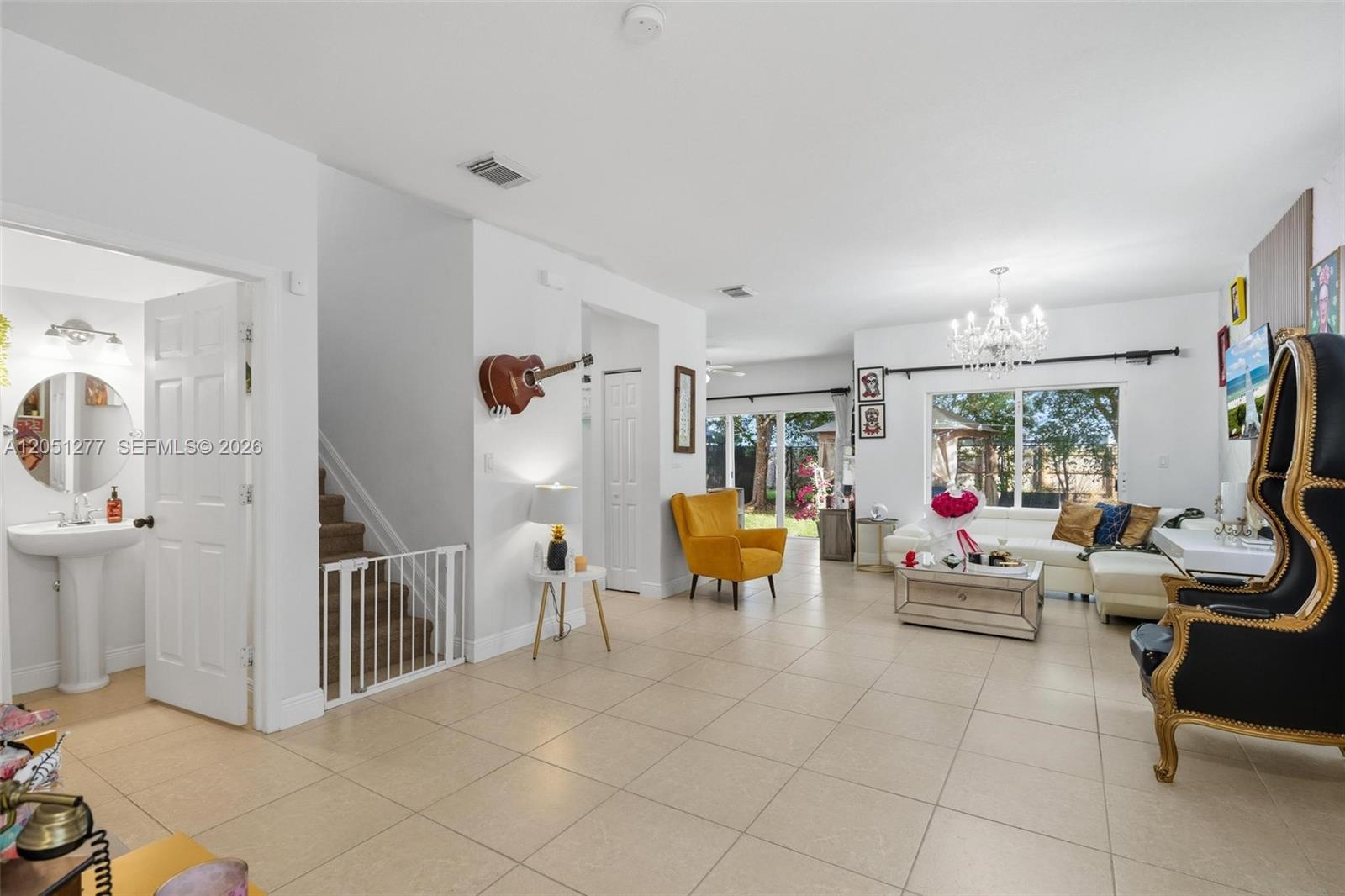 A bright living room features tile flooring, a yellow armchair, a white sofa, and a staircase — 357 NE 35th Ter, Homestead FL 33033, HOMESTEAD, FL