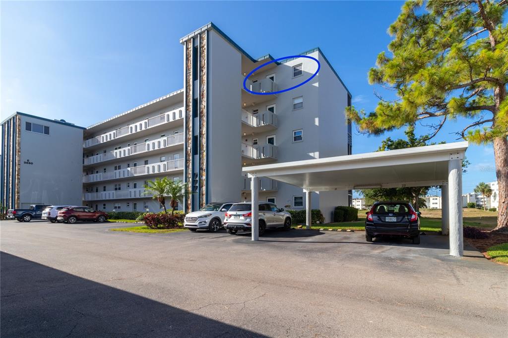 Exterior view of a multi-story apartment building with a circled top-floor balcony and parking area — 3880 IRONWOOD LANE UNIT 508E, BRADENTON, FL