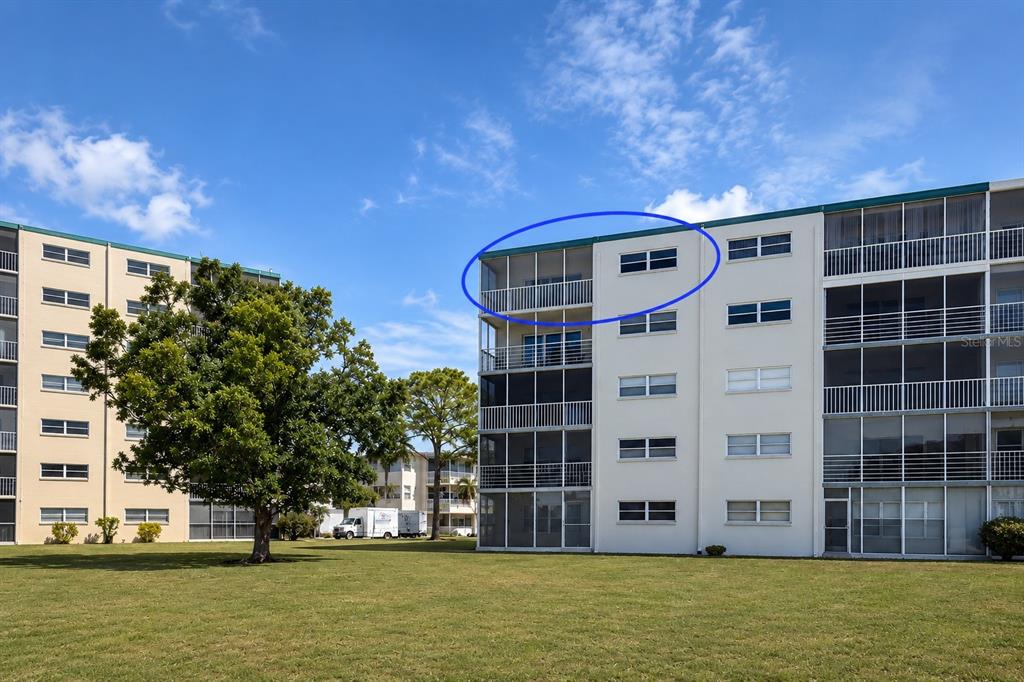 An exterior view of a multi-story apartment building with a blue circle highlighting the top-floor balcony — 3880 IRONWOOD LANE UNIT 508E, BRADENTON, FL