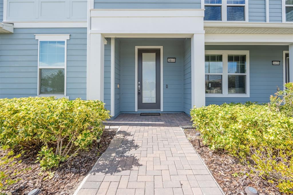 A paved walkway leads to the front entrance of a blue-sided house with bushes — 14440 ORCHID ISLAND DRIVE, ORLANDO, FL