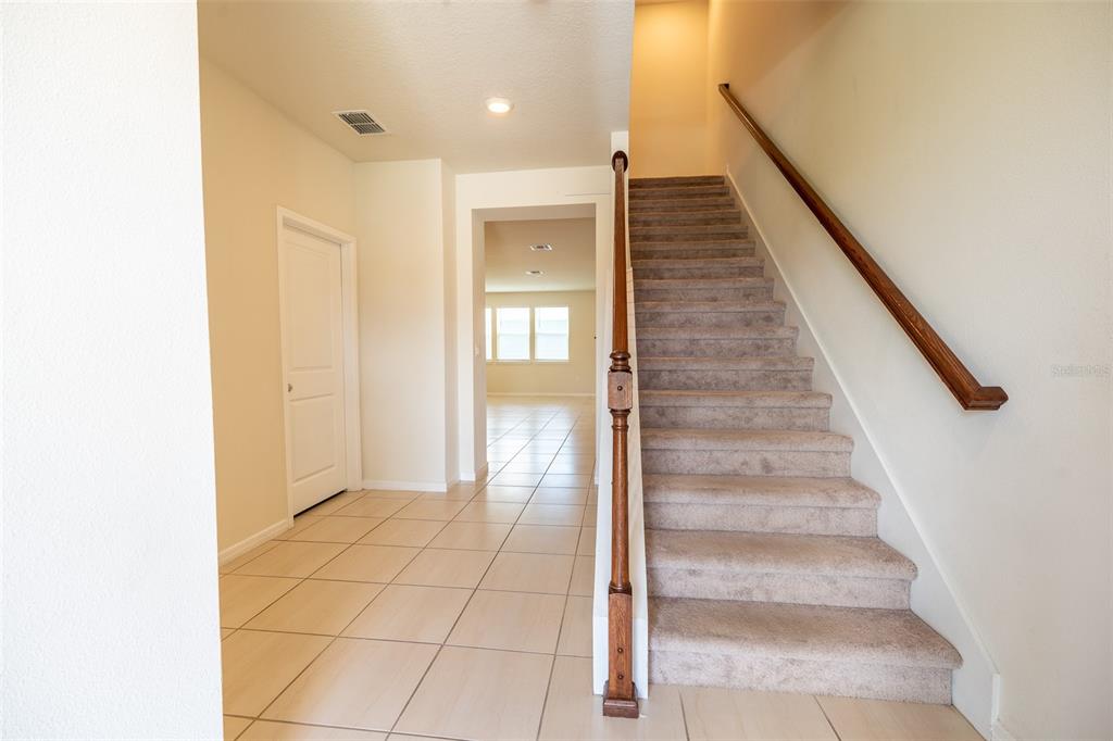 An entryway features a carpeted staircase with a wooden railing and light-colored tile flooring — 14440 ORCHID ISLAND DRIVE, ORLANDO, FL