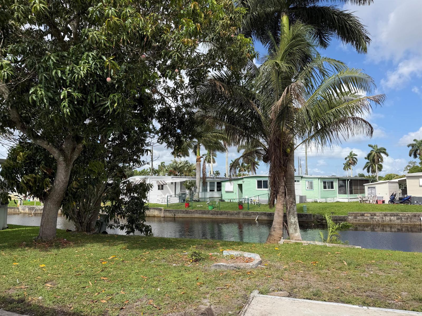 A canal separates a grassy yard with trees from a row of mobile homes — 2041 SW 84th Avenue, Davie FL 33324, DAVIE, FL