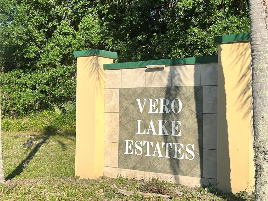 A stone monument sign for Vero Lake Estates stands in front of dense green trees — 8965 100TH AVENUE, VERO BEACH, FL