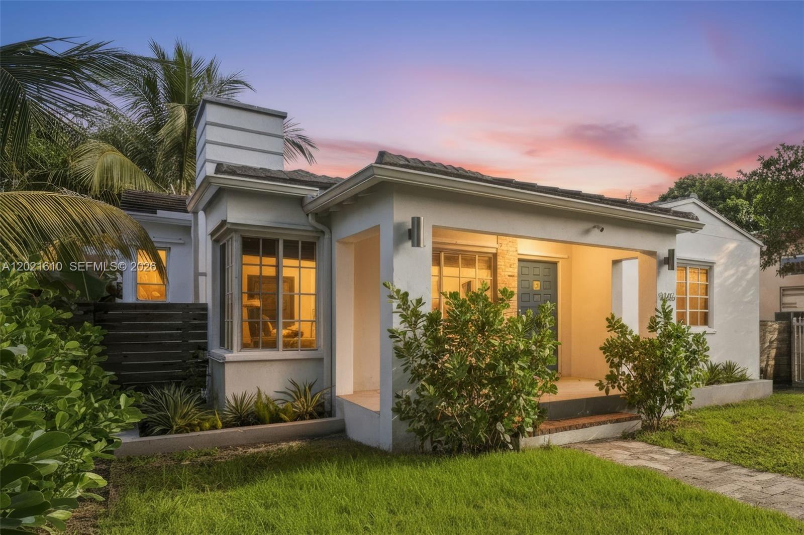 A white single-story house with a covered porch, bay window, and a sunset sky background — 555 NE 73rd St, Miami FL 33138, MIAMI, FL