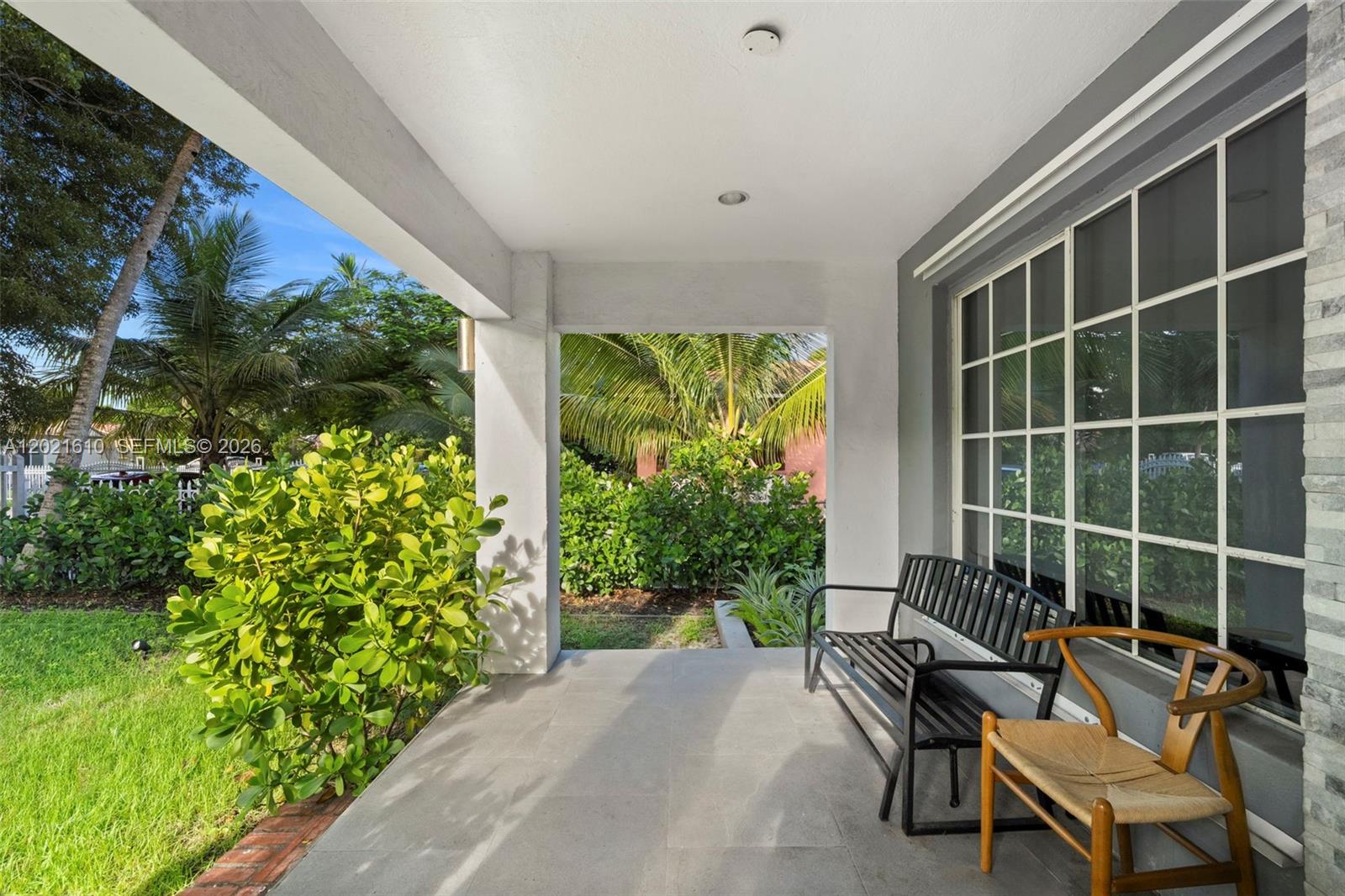 A covered porch features gray tile flooring, a black metal bench, and a wooden chair — 555 NE 73rd St, Miami FL 33138, MIAMI, FL