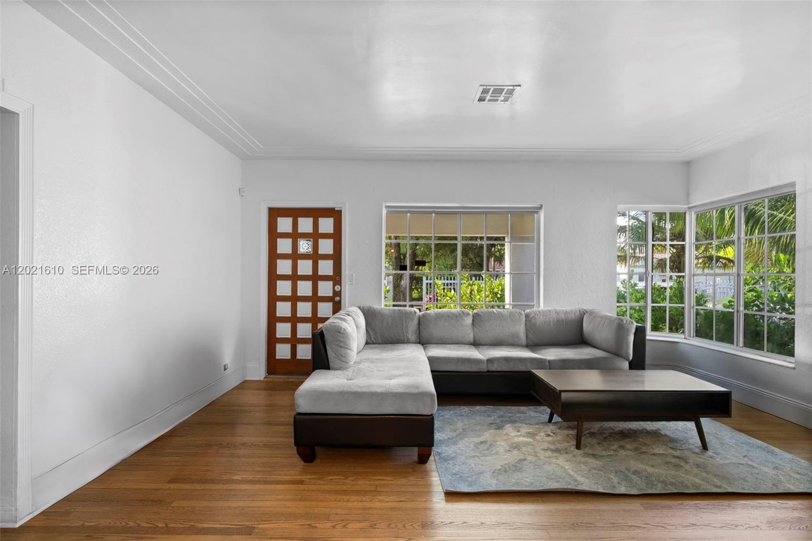 A living room features hardwood floors, a grey sectional sofa, and a wooden front door — 555 NE 73rd St, Miami FL 33138, MIAMI, FL