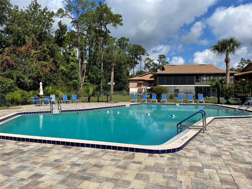 A rectangular swimming pool with blue lounge chairs sits on a stone patio outdoors — 100 SWEETGUM WOODS COURT UNIT 8D, DELTONA, FL
