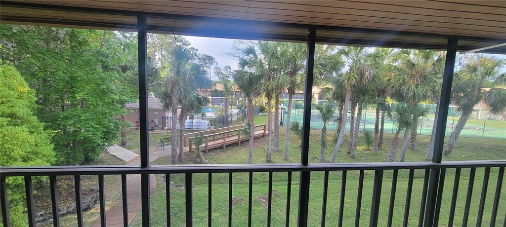 A view from a screened-in balcony overlooking a grassy area, palm trees, and tennis courts — 100 SWEETGUM WOODS COURT UNIT 8D, DELTONA, FL