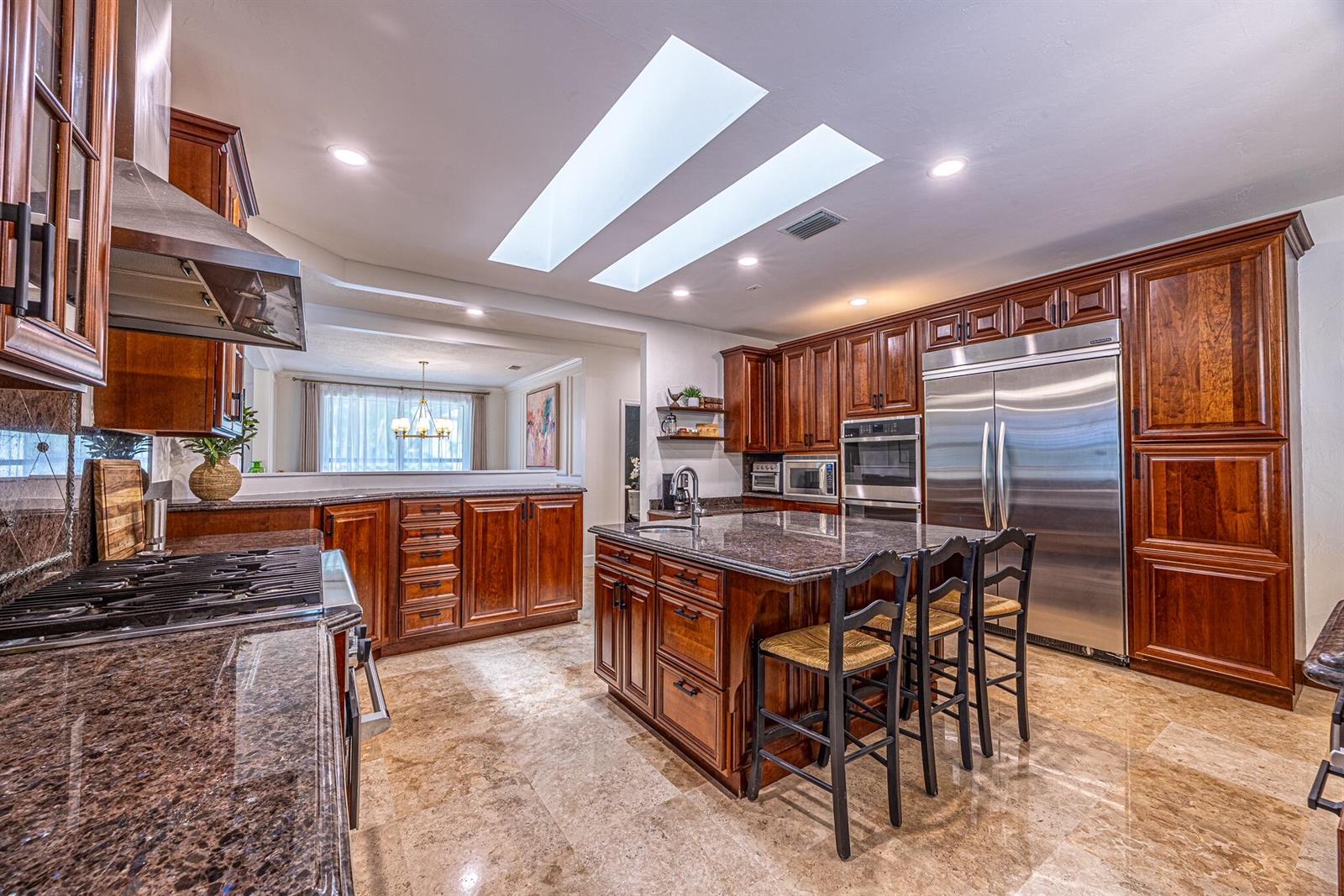 A kitchen features dark wood cabinets, granite countertops, a center island, and two large skylights — 1985 Parkside Circle S, Boca Raton FL 33486, BOCA RATON, FL