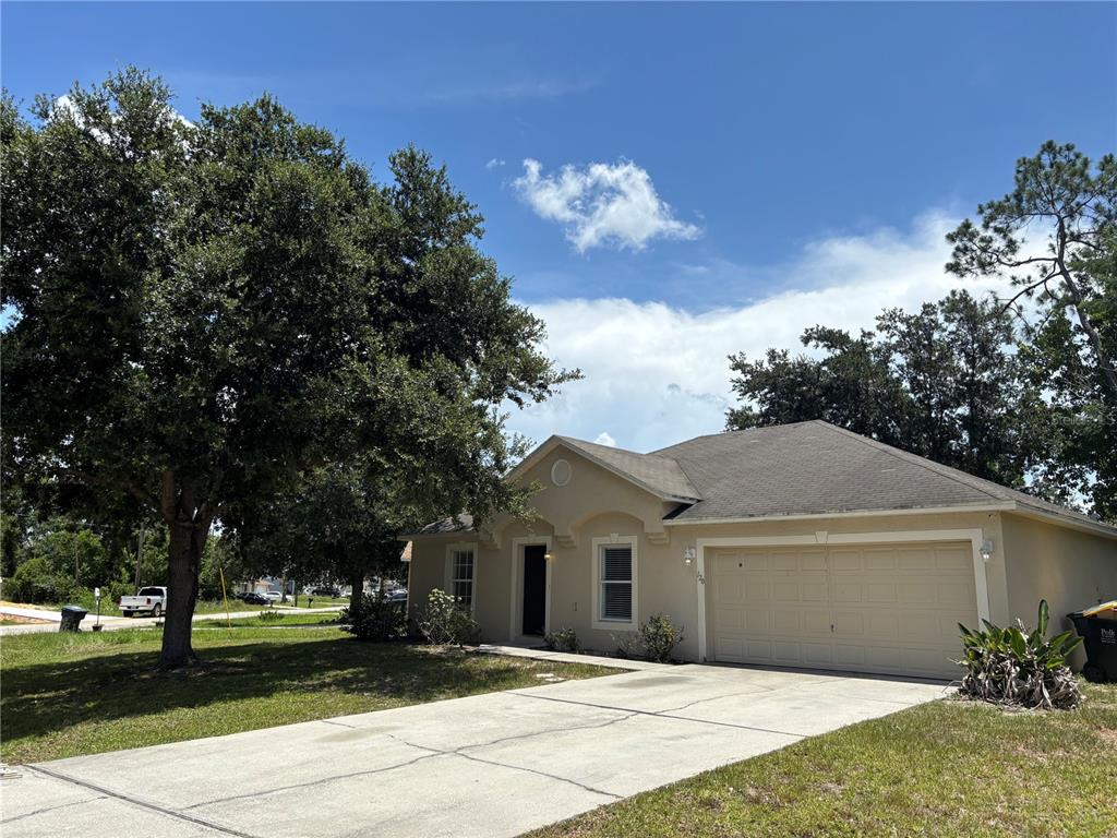 A single-story beige house with a two-car garage and a large tree in the yard — 120 SPOONBILL COURT, POINCIANA, FL