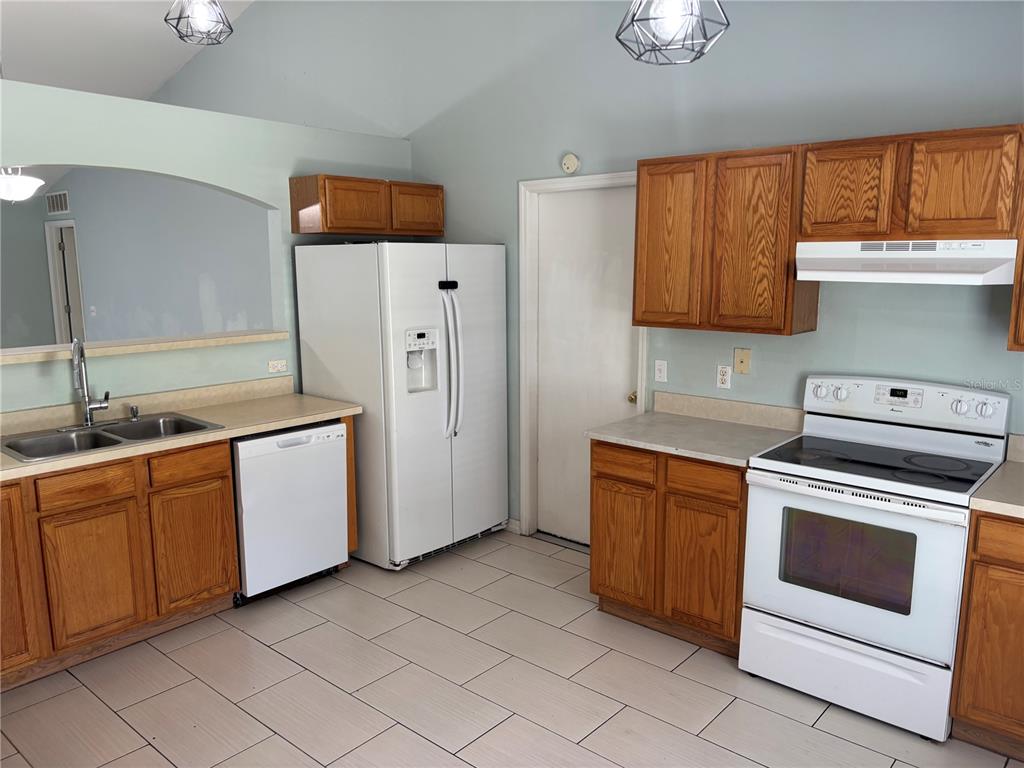 A kitchen features oak cabinets, white appliances, light-colored tile flooring, and a vaulted ceiling — 120 SPOONBILL COURT, POINCIANA, FL