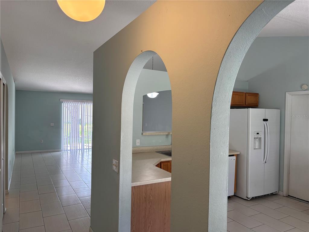 A view through an arched doorway into a kitchen with a white refrigerator and tile — 120 SPOONBILL COURT, POINCIANA, FL