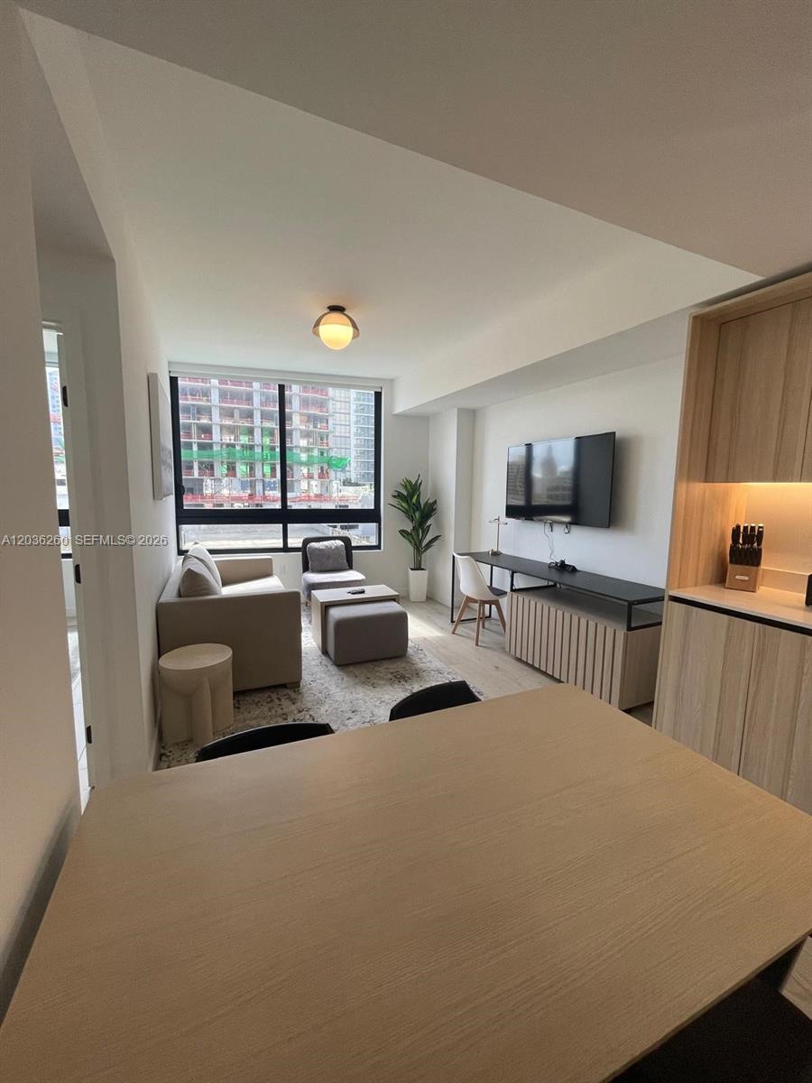 This modern living room features light wood cabinetry, a wall-mounted television, and floor-to-ceiling windows — 225 N Miami Ave # 805, Miami FL 33128, MIAMI, FL