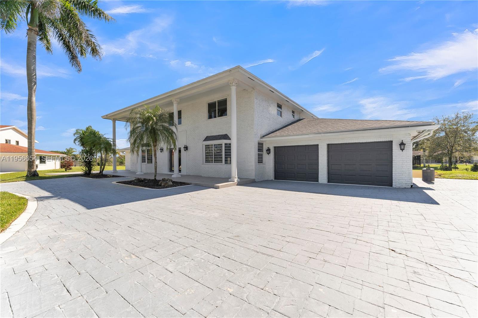 A two-story white brick house features a large paved driveway and a two-car garage — 11824 SW 43rd Ct, Davie FL 33330, DAVIE, FL