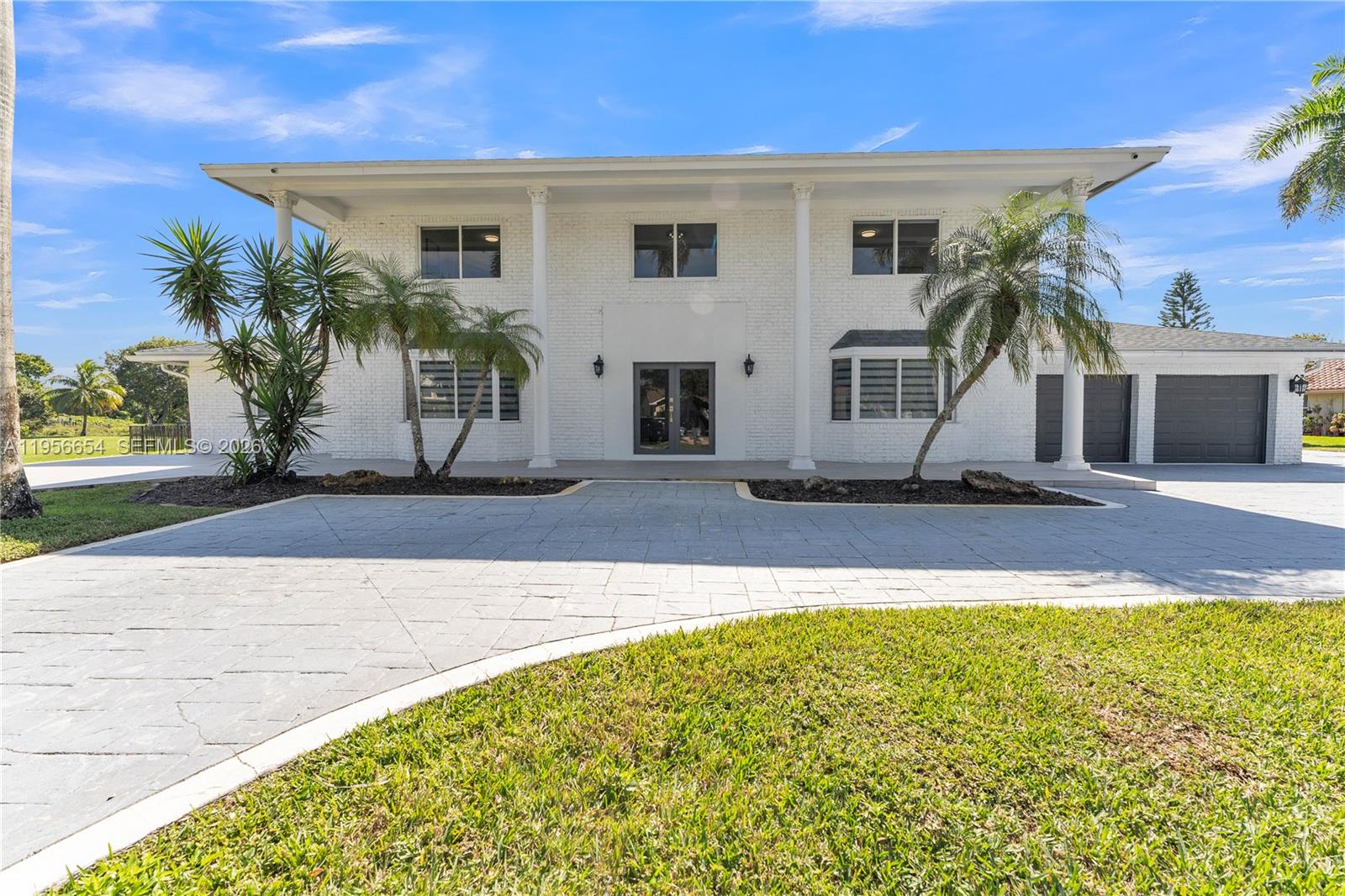 A two-story white brick house features a large paved driveway and several palm trees — 11824 SW 43rd Ct, Davie FL 33330, DAVIE, FL