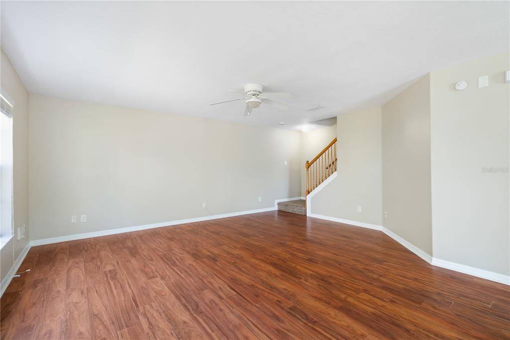 A living room with light-colored walls, wood-look flooring, a ceiling fan, and a staircase — 10932 BRICKSIDE COURT UNIT 10932, RIVERVIEW, FL