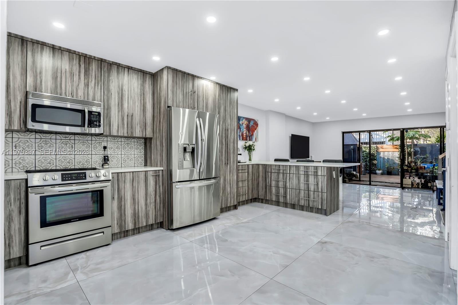 A modern kitchen features wood-grain cabinets, stainless steel appliances, and glossy light gray tile flooring — 3321 Simms St # 13B, Hollywood FL 33021, HOLLYWOOD, FL