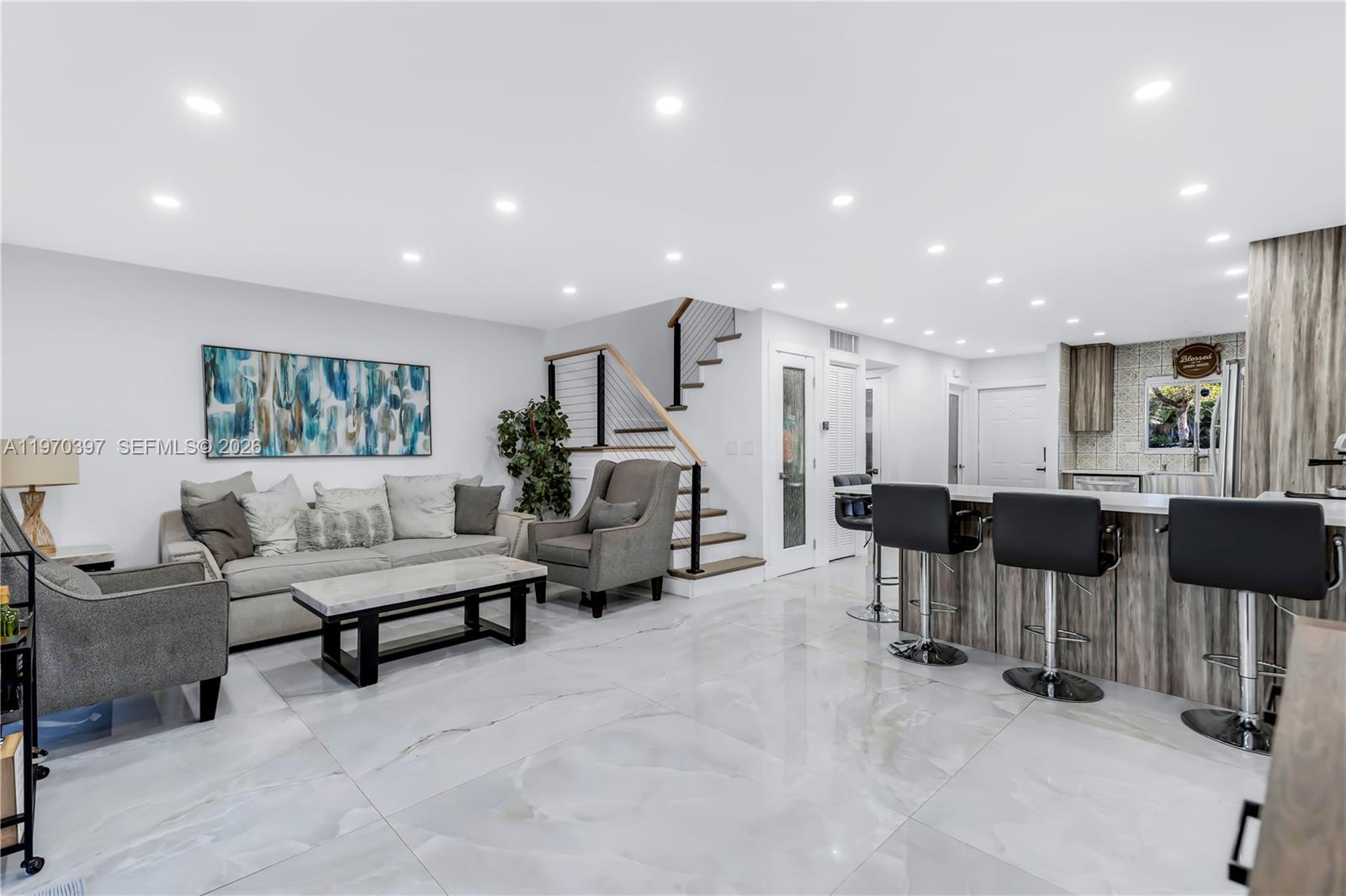 A modern living room and kitchen area features white marble floors and a wooden staircase — 3321 Simms St # 13B, Hollywood FL 33021, HOLLYWOOD, FL