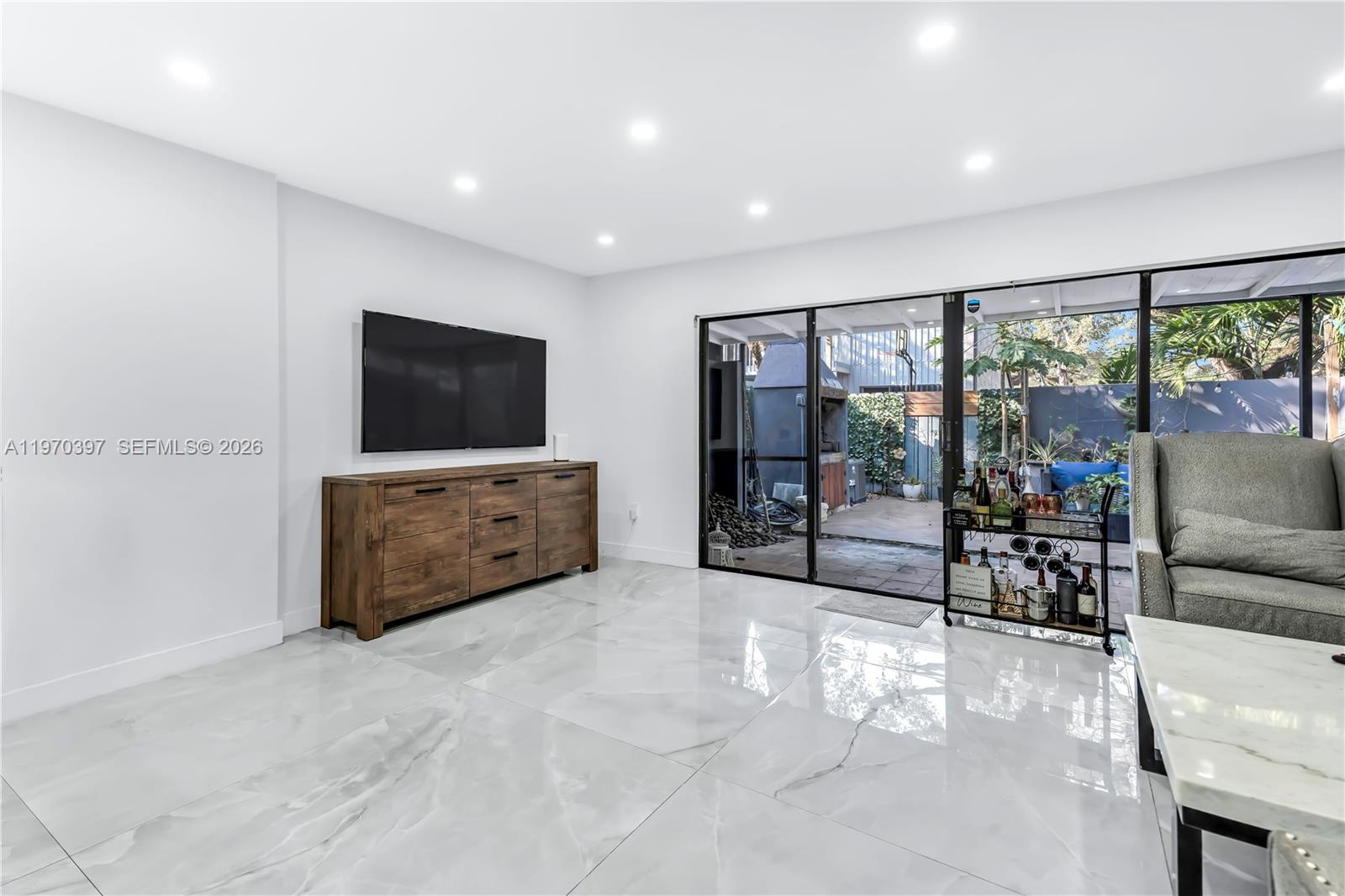 A modern living room features white marble floors, a wooden media console, and sliding glass doors — 3321 Simms St # 13B, Hollywood FL 33021, HOLLYWOOD, FL