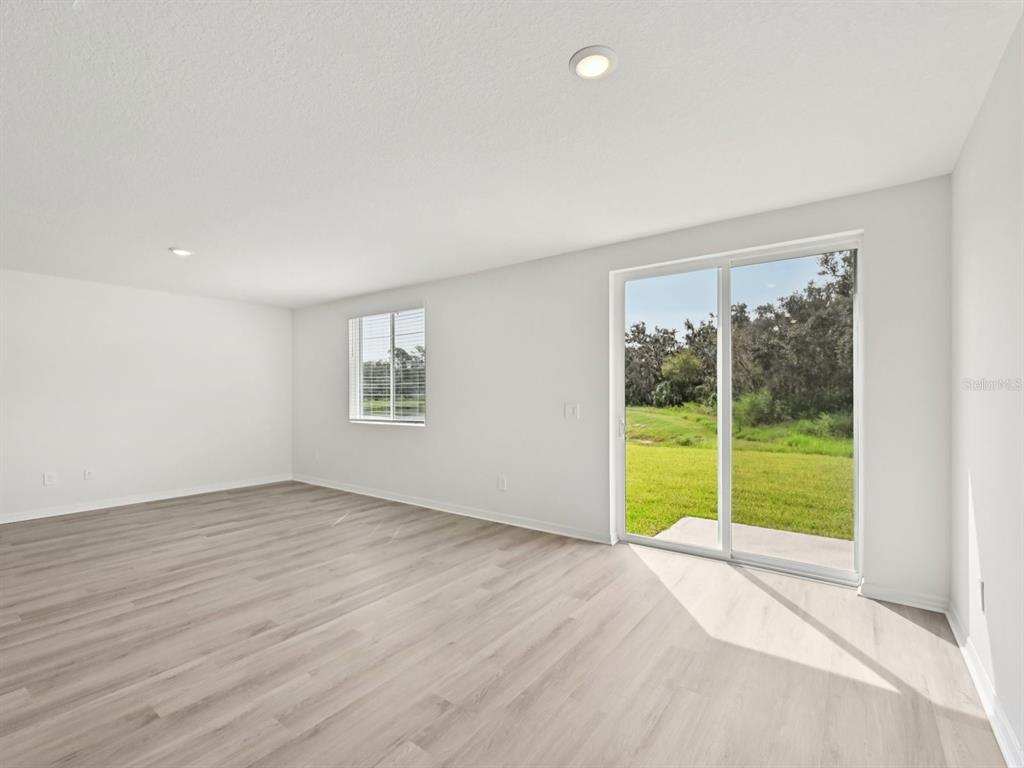 An empty room features light wood-look flooring, white walls, a window, and sliding glass doors — 1773 FOREST RUN LANE, AUBURNDALE, FL