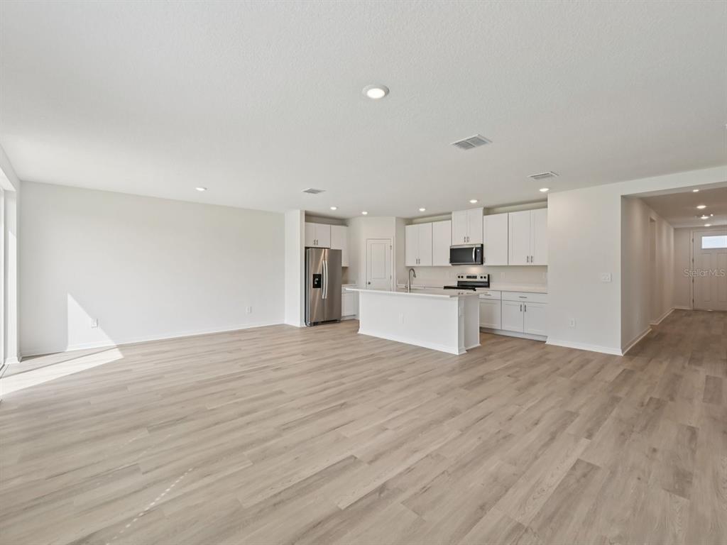 An open-concept kitchen features white cabinetry, stainless steel appliances, and light wood-look flooring — 1773 FOREST RUN LANE, AUBURNDALE, FL