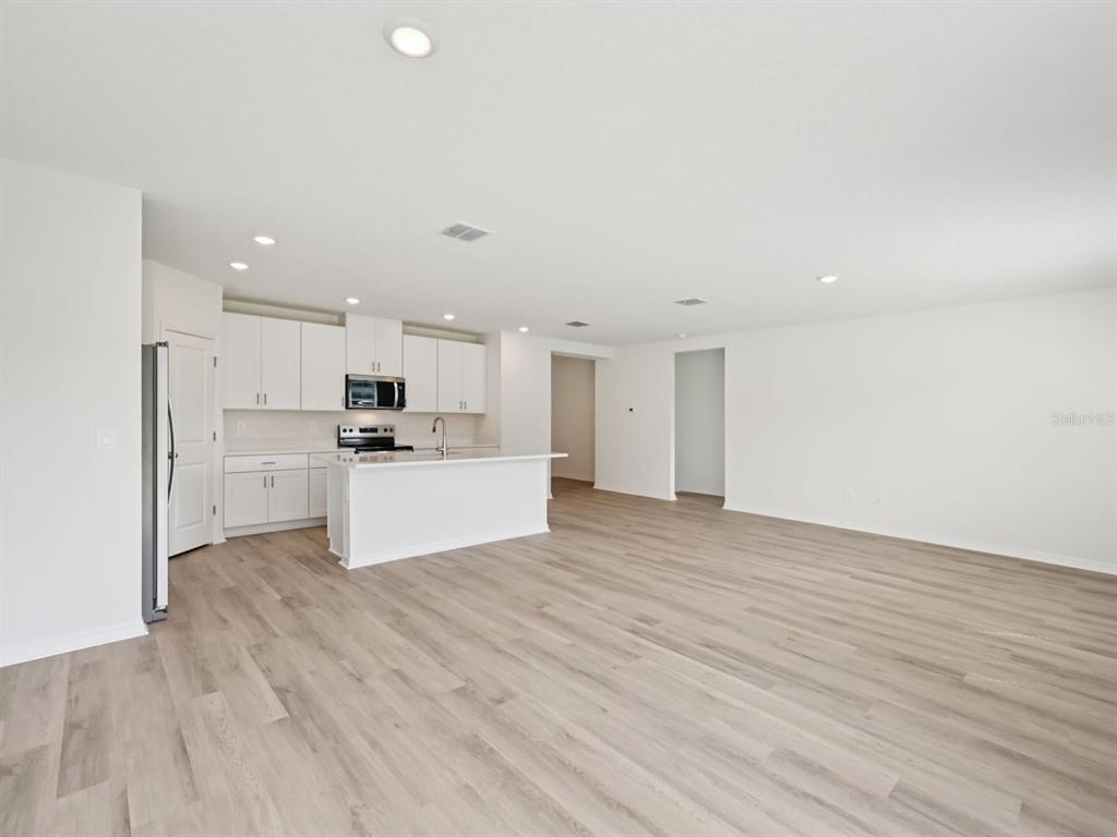 An open-concept kitchen and living area features white cabinetry, a central island, and light flooring — 1773 FOREST RUN LANE, AUBURNDALE, FL