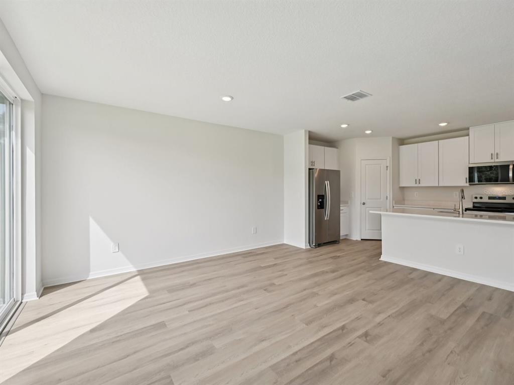 An open-concept kitchen and living area feature light wood-look flooring and white cabinetry — 1773 FOREST RUN LANE, AUBURNDALE, FL
