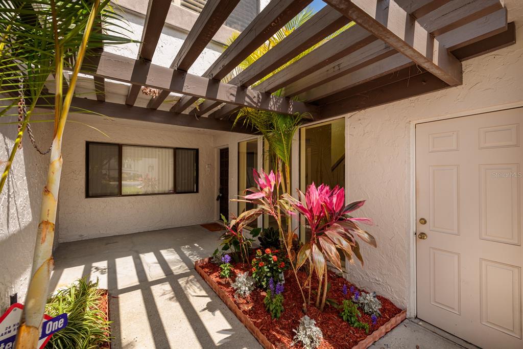 A covered entryway features a wooden pergola, a small garden bed, and a white door — 4207 FAIRWAY RUN, TAMPA, FL
