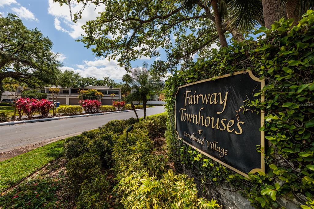 A black sign for Fairway Townhouses at Carrollwood Village stands beside a paved road — 4207 FAIRWAY RUN, TAMPA, FL