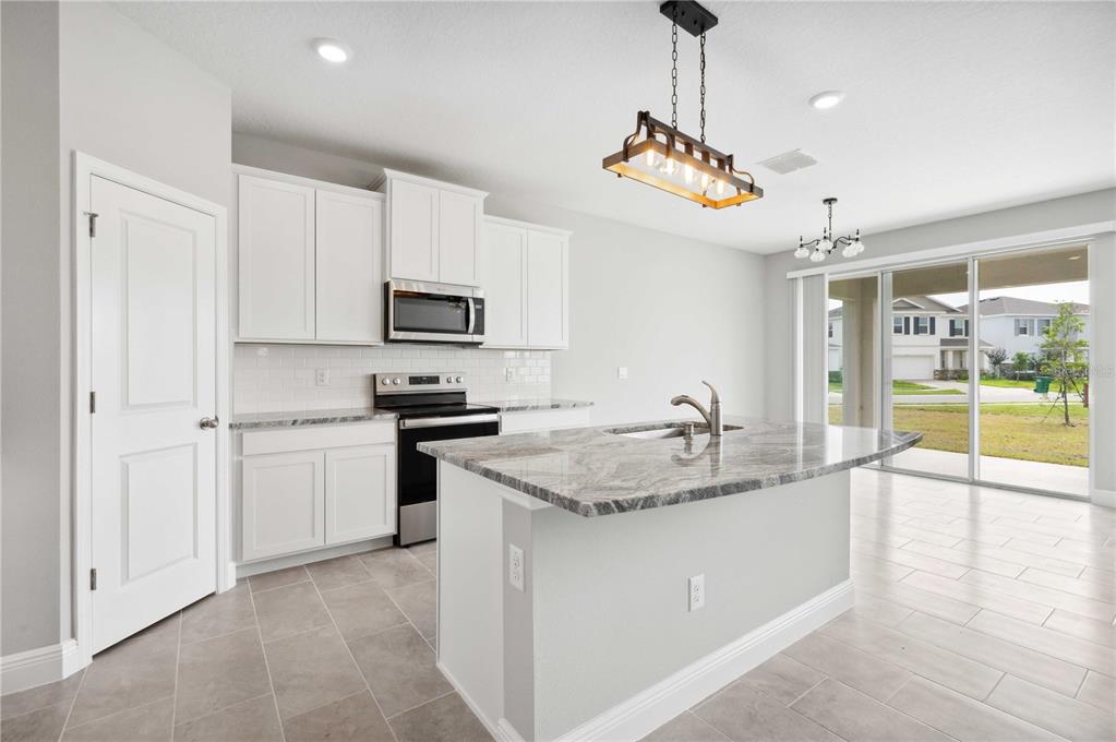 A kitchen with white cabinets, a granite-topped island, and a sliding glass door to outside — 2560 WARREN ACRES BOULEVARD, WESLEY CHAPEL, FL