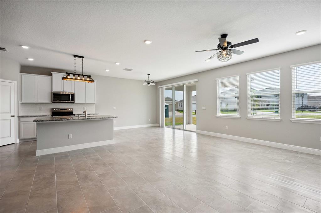 An open-concept kitchen and living area with tile flooring, white cabinets, and sliding glass doors — 2560 WARREN ACRES BOULEVARD, WESLEY CHAPEL, FL