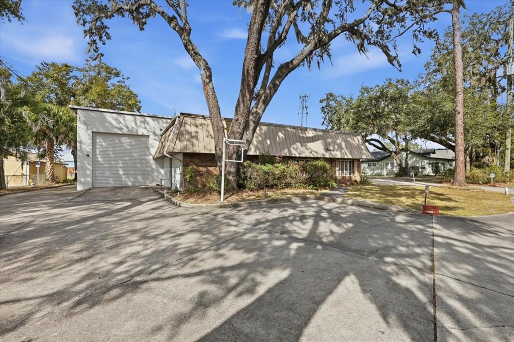 A commercial building with a roll-up garage door, tan mansard roof, and large oak trees — 1022 WILFRED DRIVE, ORLANDO, FL