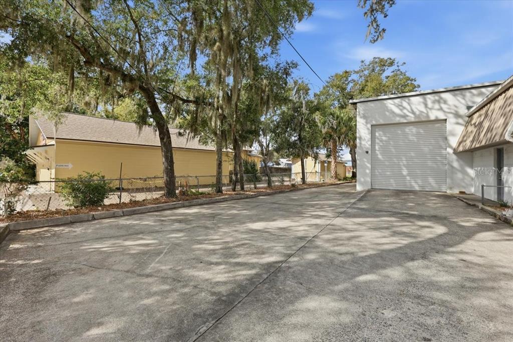 A paved driveway leads to a white industrial building with a large roll-up garage door — 1022 WILFRED DRIVE, ORLANDO, FL