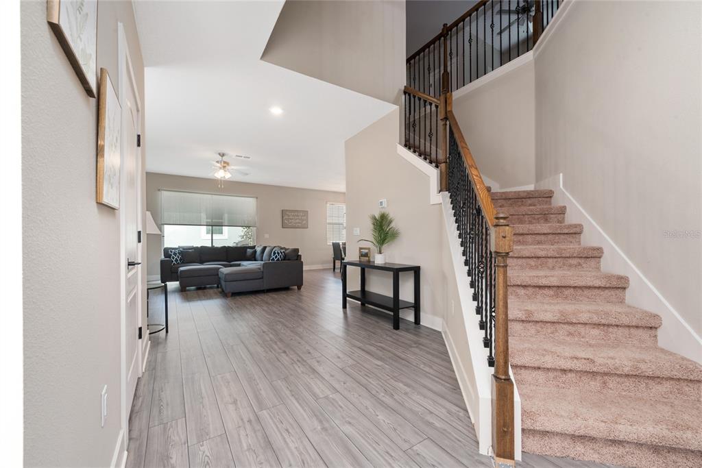An entryway features wood-look flooring, a carpeted staircase with a wooden railing, and a living room — 7955 HAVERHILL WAY, REUNION, FL