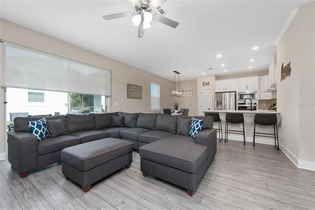 A living room with a large gray sectional sofa, open kitchen, and light wood flooring — 7955 HAVERHILL WAY, REUNION, FL