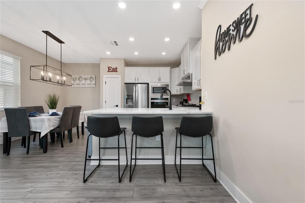 A kitchen with white cabinets, a quartz island, and three bar stools faces a dining area — 7955 HAVERHILL WAY, REUNION, FL