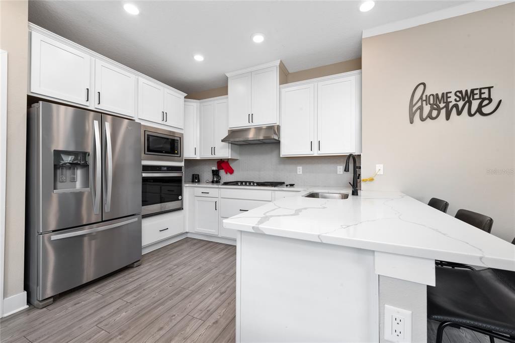 A modern kitchen features white cabinets, stainless steel appliances, and a white quartz island countertop — 7955 HAVERHILL WAY, REUNION, FL