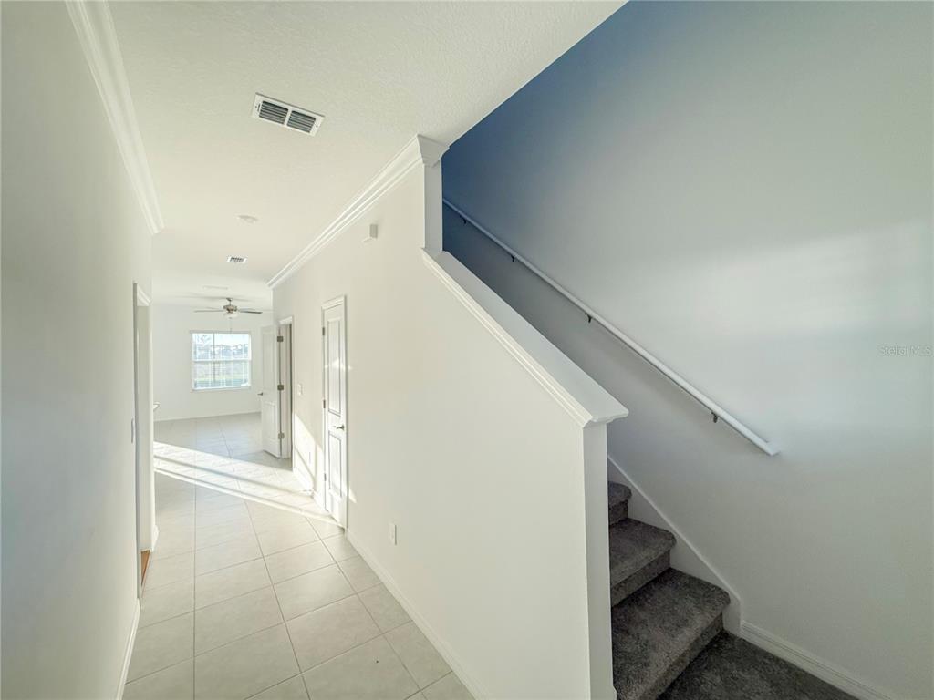 A hallway with tile flooring leads to a room with a ceiling fan and stairs — 9001 GALLANTREE PLACE, LAND O LAKES, FL