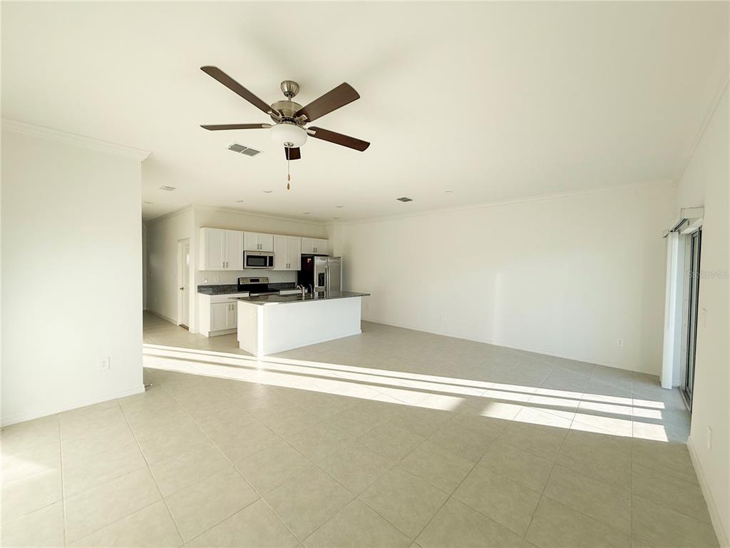An open-concept kitchen with white cabinets and a center island overlooks a tiled living area — 9001 GALLANTREE PLACE, LAND O LAKES, FL