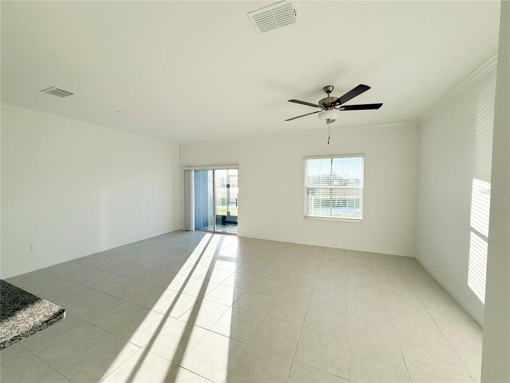 An empty living room features light tile flooring, a ceiling fan, and sliding glass doors — 9001 GALLANTREE PLACE, LAND O LAKES, FL