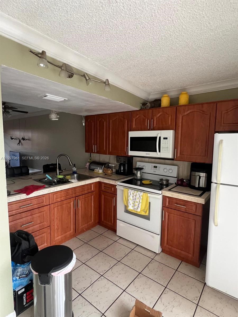 A kitchen features wood cabinets, white appliances, tile flooring, and a track lighting fixture — 1298 W 51st Pl # 29, Hialeah FL 33012, HIALEAH, FL