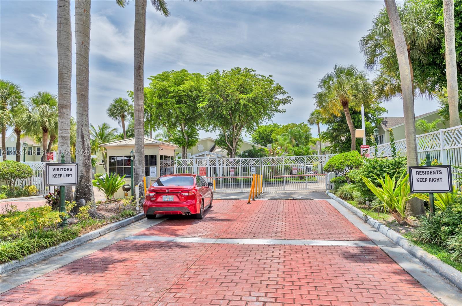 A red car is parked at a gated community entrance with separate lanes for visitors and residents — 17485 NW 67th Ct # 21, Hialeah FL 33015, HIALEAH, FL