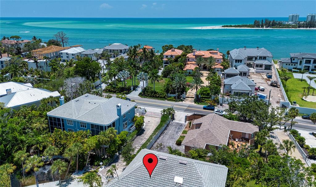 An aerial view shows a coastal neighborhood with houses, lush vegetation, and a turquoise ocean — 3915 SOMERSET DRIVE UNIT 9, SARASOTA, FL