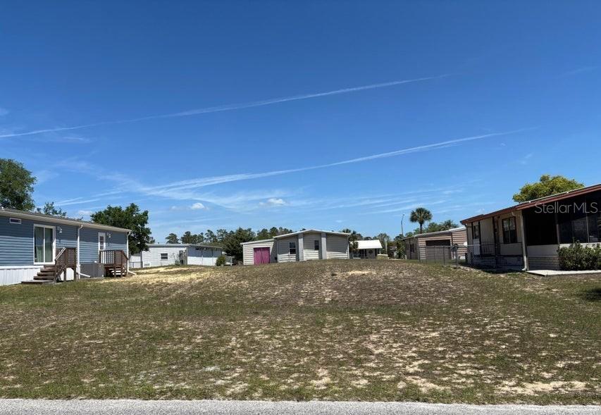 A vacant, grassy lot sits between two manufactured homes under a clear blue sky — 14405 DIABLO DRIVE, BROOKSVILLE, FL