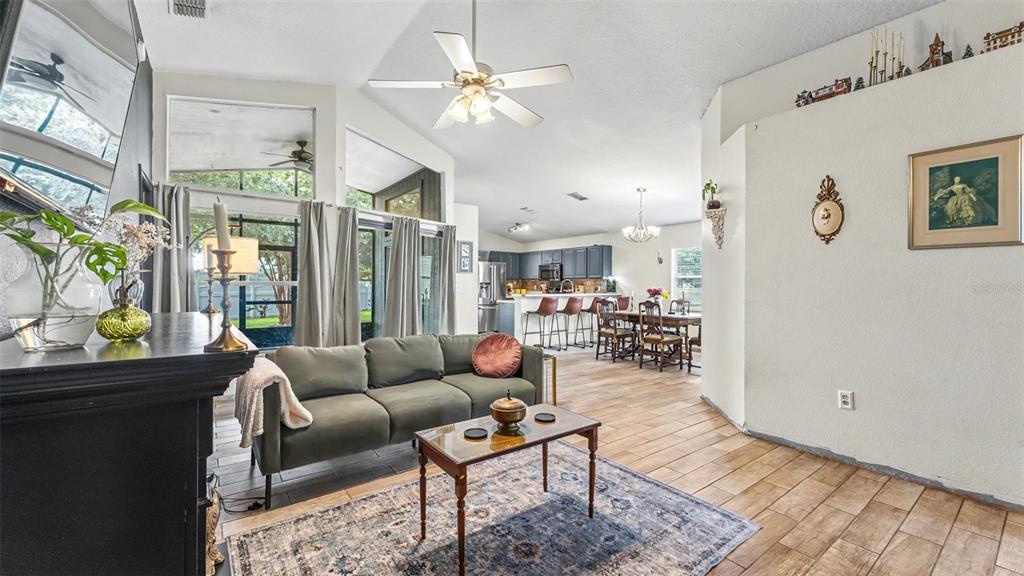 A living room with a green sofa, wood-look tile floors, and an open kitchen beyond — 2723 SUNDANCE CIRCLE, MULBERRY, FL