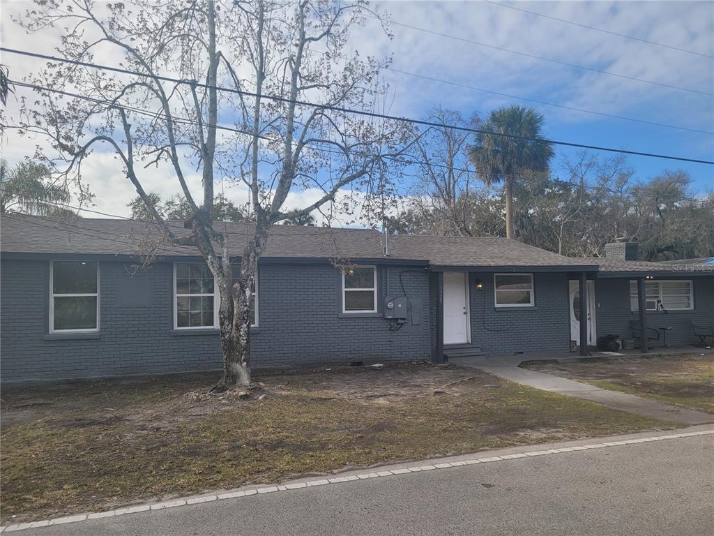 A single-story gray brick house with a white front door and a large bare tree — 1320 S OLEANDER AVENUE, SANFORD, FL