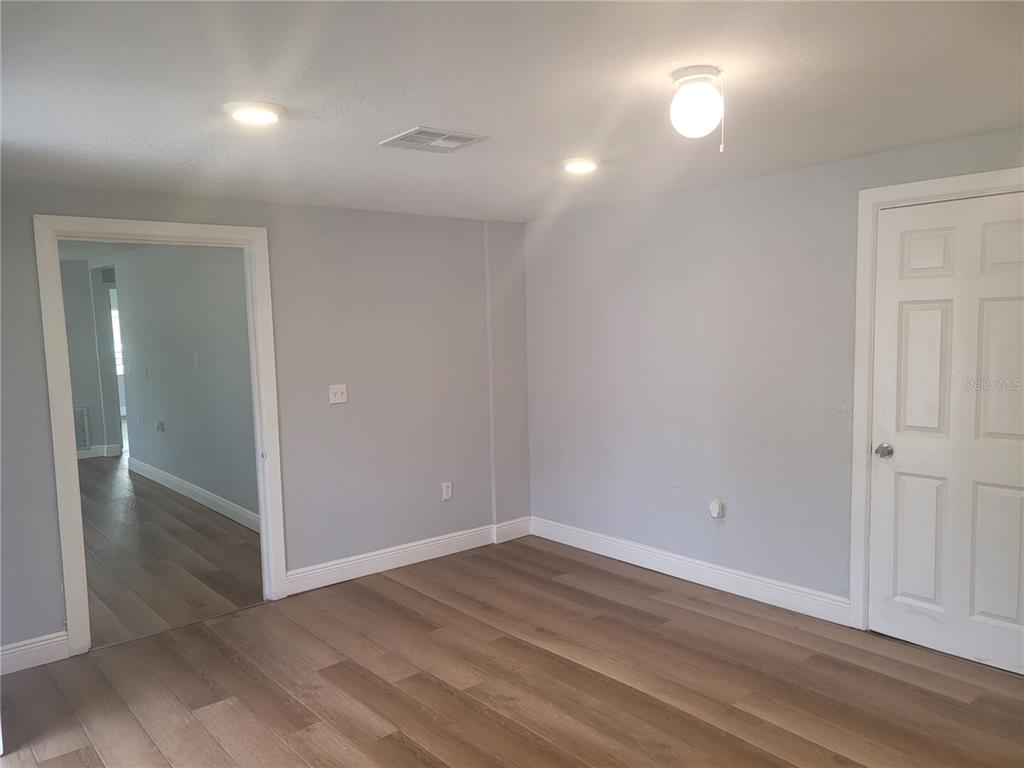 An empty room with light gray walls, wood-look flooring, a doorway, and a white door — 1320 S OLEANDER AVENUE, SANFORD, FL